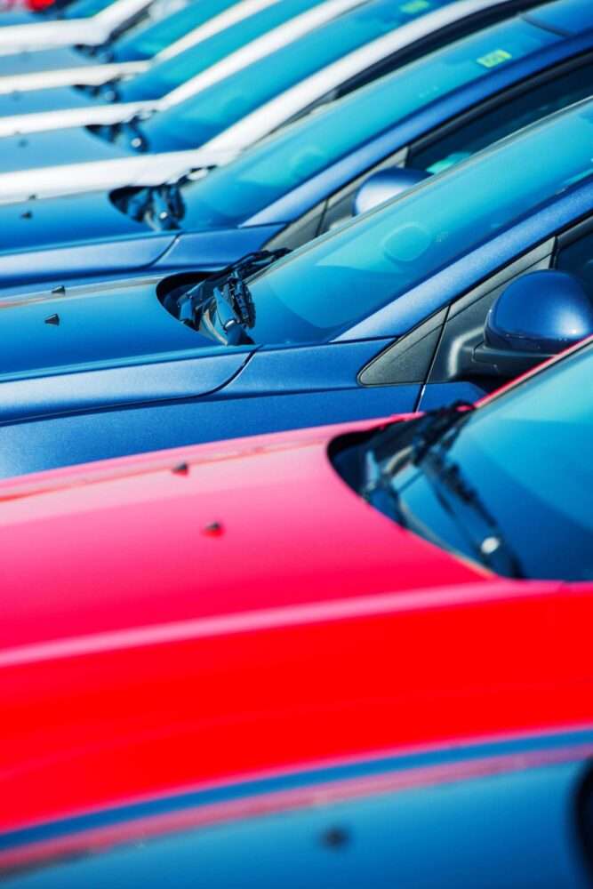 auto verkaufen - Eine Reihe geparkter Autos in verschiedenen Farben, darunter Blau, Rot und Weiß, aus seitlicher Perspektive betrachtet. Der Fokus liegt auf den Motorhauben und Windschutzscheiben, auf deren Oberflächen Lichtreflexionen sichtbar sind. - Gebrauchtwagen Autohändler
